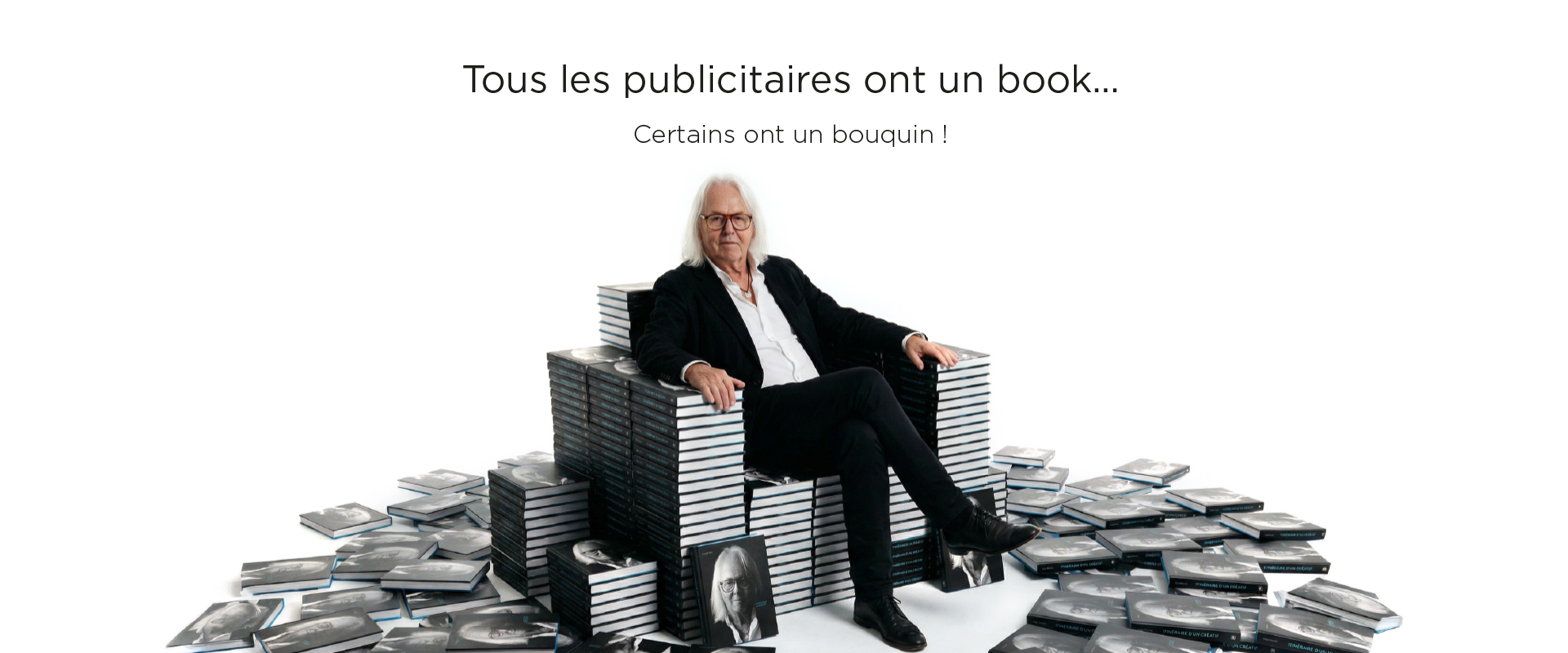 Tous les publicitaires ont un book, certains ont un bouquin - Roland Anstett assis sur des piles de livres